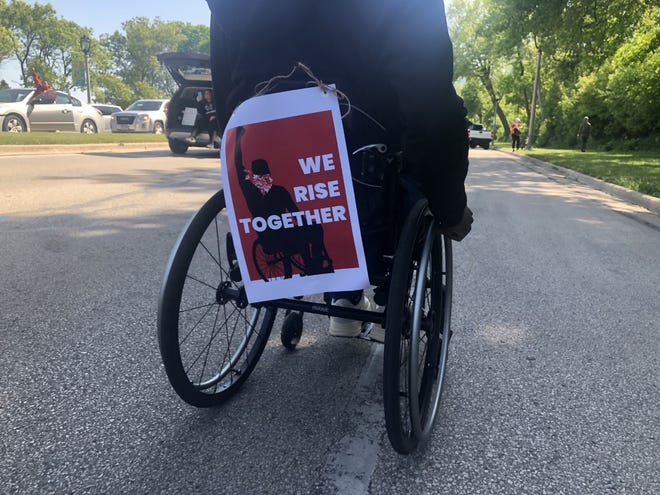 Poster that says "We rise together" attached to the back of a wheelchair