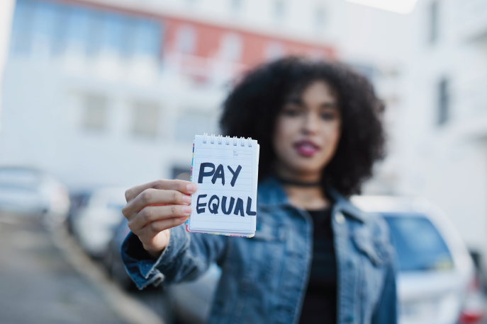 Woman holding up a piece of paper that says "Pay Equal"