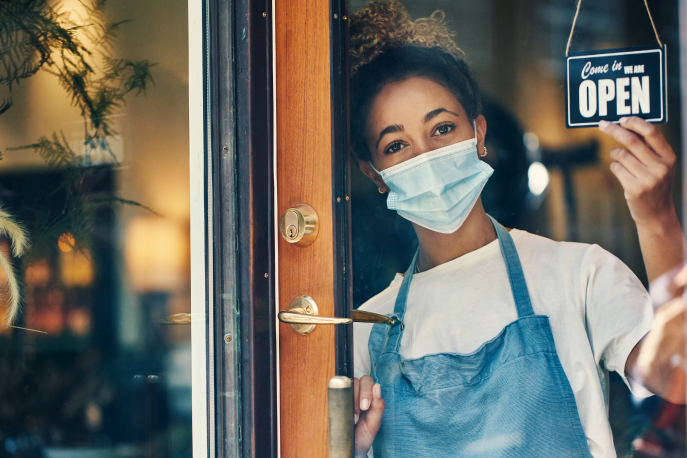 Woman wearing a mask putting up and OPEN sign in a restaurant