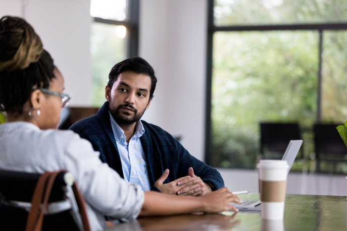 Image of man and woman sitting together and talking in the workplace.