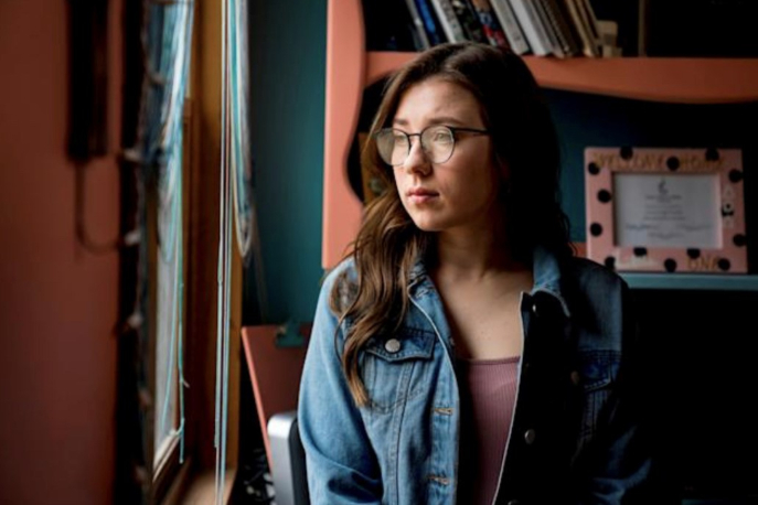 Mackenzie Loesch leaning against a bookcase, looking to the side