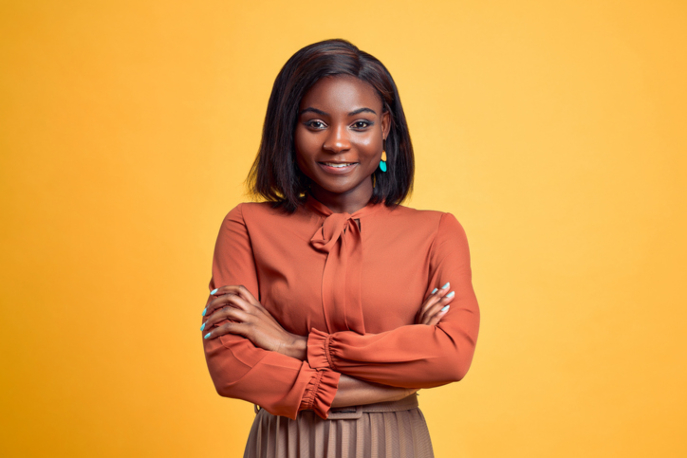 Black woman in orange blouse, smiling at the camera in front of yellow background