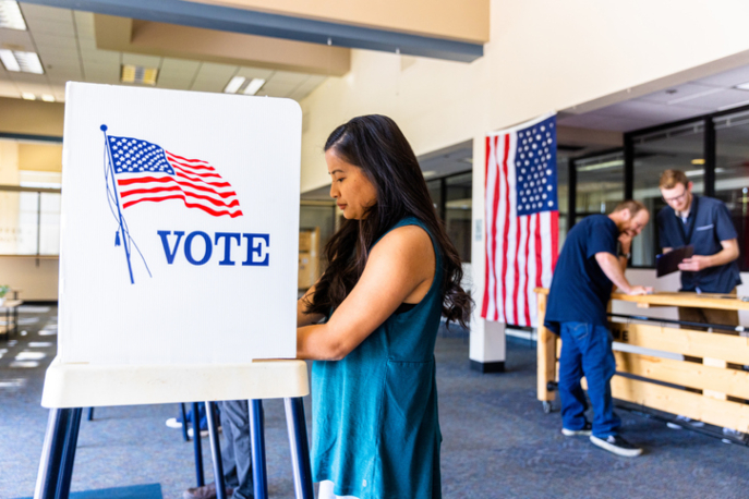 Woman in blue shirt voting in a voting booth.