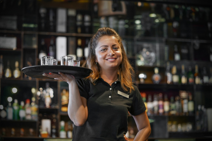 Waitress smiling at camera with one hand holding up tray of glasses.