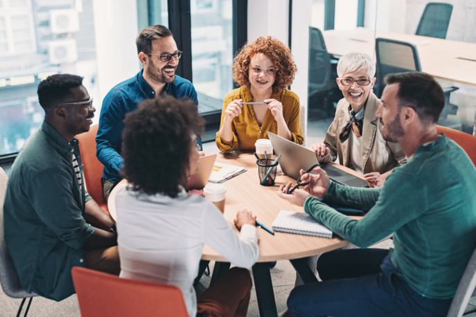 Team of young adults conducting a meeting around a circular table, smiling.