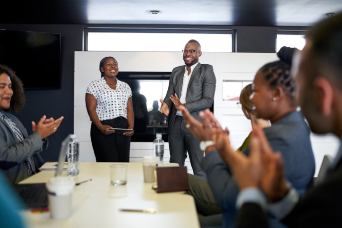 A Black man and woman leading a work meeting to a majority-Black team.
