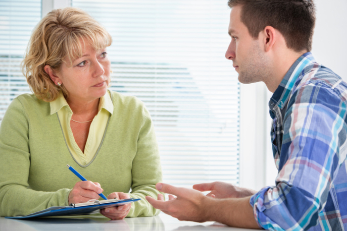 Teenage boy talking to adult woman which a clipboard who is listening attentively.