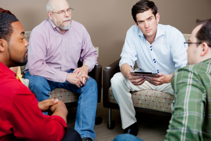 Four men seated in a circle, intently listening to each other.