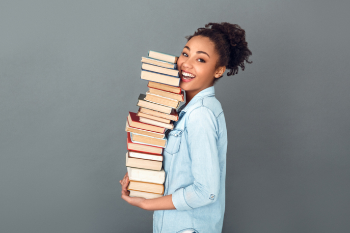 Young African American woman isolated on grey wall holding books.