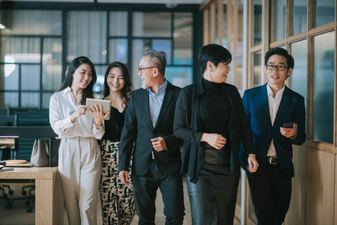 Group of Asian workplace professionals having a discussion while walking toward camera.