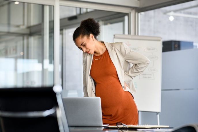 Pregnant Black business woman in office looking at a computer.