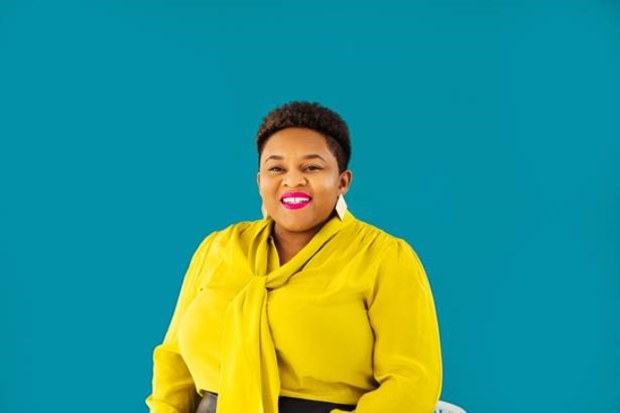 Black woman with short hair and a yellow blouse on a teal background.