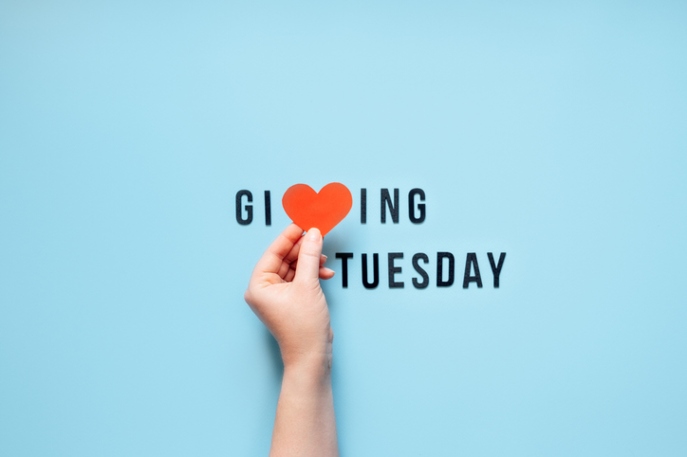 "Giving Tuesday" in black font on light blue background. The "v" is a heart held by a white hand coming in the frame.