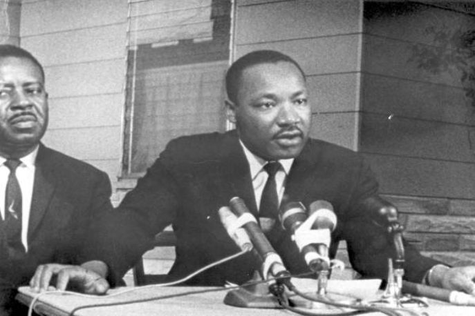 Black and white image of Martin Luther King Jr. speaking at a press conference