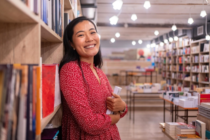 Asian woman in a red dress against a library bookshelf, smiling.