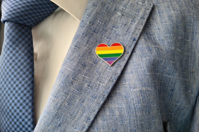 Close up of a gay pride heart pin on a business suit.