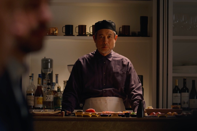 Older gentleman working as a chef, looking at someone seated disapprovingly