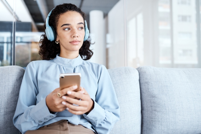 Woman in business outfits holding a phone and listening to her headphones.