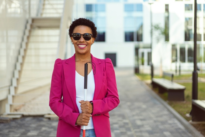 A blind businesswoman wearing dark glasses and holding a white cane, smiling at the camera.