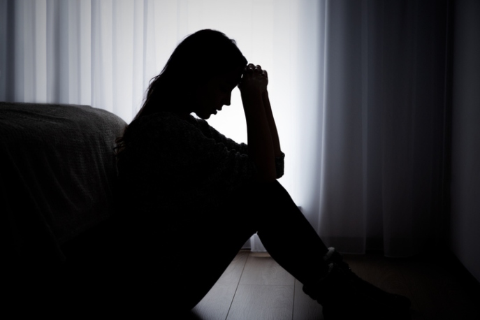 Silhouette of woman in darkness holding her head.
