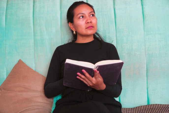 Young Native American woman reading a book and thinking on a turquoise sofa