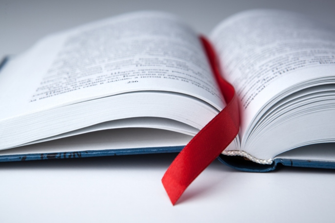 open book on a gray table with a red ribbon bookmark close up