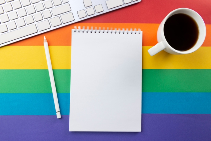 Gay pride flag with white mug, keyboard, and notepad on top.